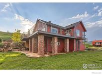 Stunning raised red home with a large deck supported by brick pillars, surrounded by lush greenery and a stone staircase at 8241 N Foothills Hwy, Boulder, CO 80302