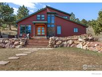 Stunning two-story home with a unique red exterior, stone accents, and a welcoming wooden arched doorway at 8543 Middle Fork Rd, Boulder, CO 80302