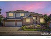 Two-story brick home featuring a three-car garage, manicured lawn, and professional landscaping at 16261 W Ellsworth Ave, Golden, CO 80401