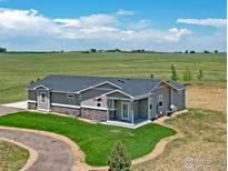 Beautiful single-story home with well-manicured lawn and circular driveway on a clear sunny day at 16527 Fairbanks N Rd, Platteville, CO 80651