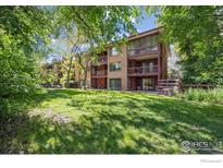 Large, landscaped backyard with mature trees and a multi-story brick apartment building featuring balconies at 715 Arapahoe Ave # 2, Boulder, CO 80302