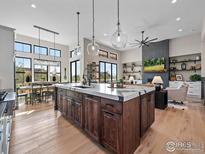 Spacious kitchen island boasts a marble countertop, dark wood cabinets, pendant lighting, and wood flooring at 1255 Eliza Ave, Berthoud, CO 80513