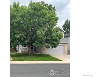 Charming two-story home with mature tree, gray siding, brick accents, and attached two car garage at 6924 Quigley Cir, Firestone, CO 80504