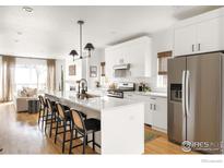 Bright white kitchen with stainless steel appliances, large island, and a view into the adjacent living space at 3422 S Grant St, Englewood, CO 80113