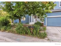 Charming blue two-story home featuring a covered front porch, lush greenery, and an attached garage at 1993 S Fork Dr, Lafayette, CO 80026