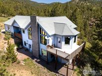 Stunning exterior view of a light blue home with a large deck and a stone chimney set among trees at 237 Puma Dr, Boulder, CO 80302