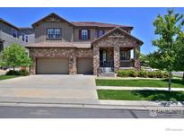 Charming two-story home with a stone and wood exterior, well-manicured lawn, and a two-car garage at 15958 Humboldt Peak Dr, Broomfield, CO 80023