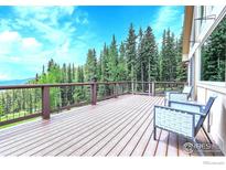 Spacious wooden deck with railing and chairs surrounded by trees, offering scenic views of the landscape at 1176 Raven Ridge Rd, Idaho Springs, CO 80452