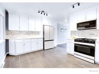Updated kitchen features white cabinets, modern appliances, tile backsplash, and tile floors at 8030 Ogden St, Denver, CO 80229