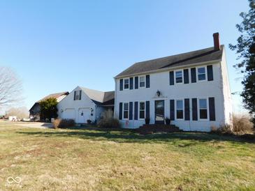 Classic two-story home with shutters, attached garage, and mature trees under a brilliant blue sky at 13205 E Legal Tender Rd, Columbus, IN 47203