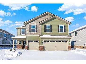 Two-story home featuring sage-green siding, stone accents, black shutters, and a two-car garage on a snow-covered lawn at 3834 Andean Dr, Bargersville, IN 46106