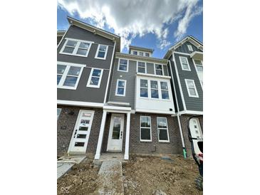 New construction gray townhomes with brick foundations beneath a partly cloudy sky, landscaping to come at 7340 W County Road 600 Rd, McCordsville, IN 46055