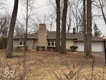 Ranch style home features a stone chimney and two-car garage nestled among mature trees at 4621 E 37Th St, Indianapolis, IN 46218