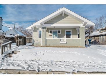 Charming craftsman home with a light green exterior, covered porch and snow covered yard at 4724 E New York St, Indianapolis, IN 46201