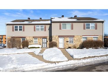 Tan siding duplex with stone accents, snowy front yard, and walkways at 2634 Country Estates Dr # 17, Indianapolis, IN 46227