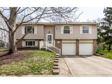 Split-level home with tan siding, white trim, attached two-car garage, and charming front yard at 9229 Thrushwood Ln, Indianapolis, IN 46250