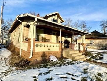 Tan house with front porch, steps, and small yard with snow at 808 S Burlington Dr, Muncie, IN 47302