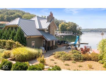 Beautiful waterfront home featuring a stone chimney, metal roof, patio, and private dock at 10841 W Grandview Dr, Columbus, IN 47201