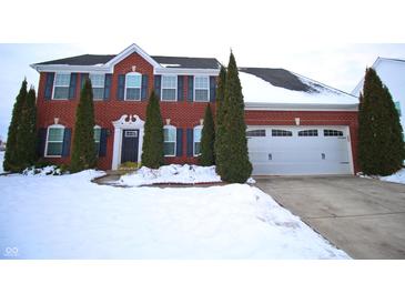 Charming red brick two-story home with a two car garage and evergreen trees in a snowy landscape at 1169 Richmond Ln, Greenwood, IN 46143