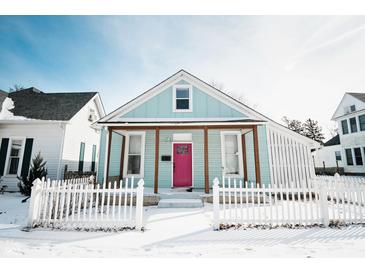 Charming home featuring a covered porch, pink front door, and white picket fence, all surrounded by a blanket of fresh snow at 205 S Market St, Thorntown, IN 46071