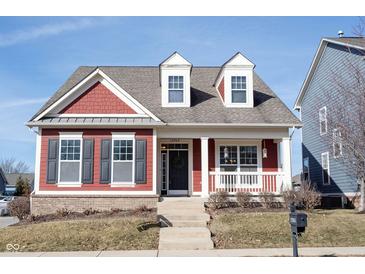 Charming two-story red home with inviting front porch and manicured lawn on a sunny day at 12964 Walbeck Dr, Fishers, IN 46037