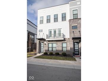 A modern three-story townhome with white siding, a grey brick base, and a small black railing balcony at 9748 Junction Station, Fishers, IN 46037