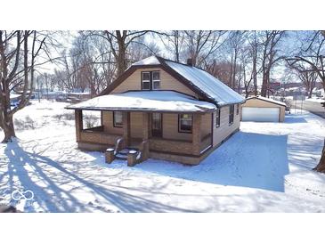 A cozy single-story home with a covered porch and detached garage sits amidst a snow-covered landscape and bare trees at 210 S West St, Paragon, IN 46166