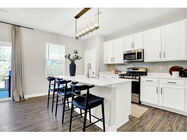 Modern kitchen featuring white cabinets, stainless steel appliances, a spacious island and hardwood flooring at 8148 Ebaugh Dr, Camby, IN 46113
