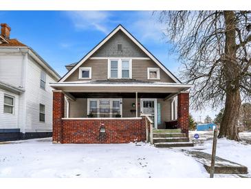 Charming two-story home featuring a welcoming front porch with brick accents and snow-covered yard at 2401 N Olney St, Indianapolis, IN 46218
