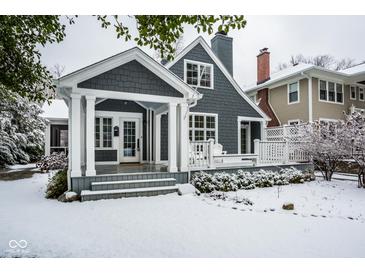 Charming gray home featuring a covered porch, white columns, and manicured landscaping dusted with snow at 5736 Central Ave, Indianapolis, IN 46220