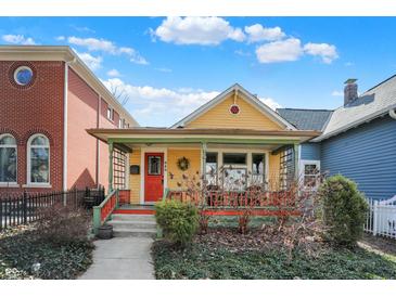 Charming yellow home features a cozy front porch, red door, and well-maintained landscaping at 645 E 9Th St, Indianapolis, IN 46202
