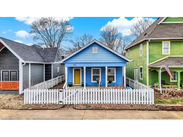 Charming blue home featuring a cozy front porch, bright yellow door, and white picket fence at 912 Harlan St, Indianapolis, IN 46203