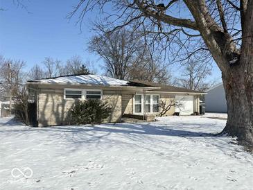 Charming one-story home with stone facade and attached garage, surrounded by a snow-covered yard and mature trees at 2104 W Barcelona Dr, Muncie, IN 47304