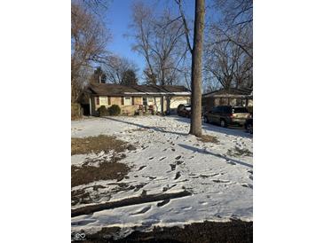 Cozy home featuring a snow-covered front yard and mature trees offering shade and privacy at 1945 N Audubon Rd, Indianapolis, IN 46218
