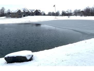 Winter view of home's pond covered in partial ice with luxury home and flagpole in the background at 9615 N County Road 150 E Rd, Pittsboro, IN 46167