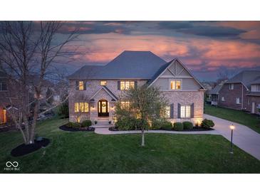 Charming two-story brick home with a manicured lawn and mature trees under a vibrant sunset sky at 10802 Giselle Way, Fishers, IN 46040