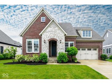Charming brick home featuring a stone facade, manicured lawn, and a welcoming three-car garage at 12167 Ams Run, Carmel, IN 46032