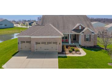 Beautiful brick home featuring a three-car garage, covered porch, and manicured lawn near a pond at 9559 Summer Hollow Dr, Fishers, IN 46037