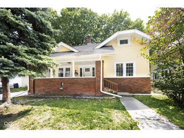 Charming yellow two-story home featuring a brick foundation, covered front porch, and well-maintained lawn at 415 Ruskin Pl, Indianapolis, IN 46205