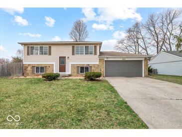 Split-level home showcasing a front yard, a two-car garage, and a combination of stone and siding at 4448 Aristocrat Cir, Indianapolis, IN 46235