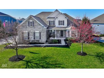 Charming two-story home featuring a manicured lawn and detailed brickwork and a front yard tree in full bloom at 13875 Ambria Dr, McCordsville, IN 46055