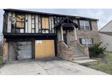 View of severely damaged two-story home with boarded up windows and missing siding, evidence of fire and water damage visible at 6009 Tammin Dr, Indianapolis, IN 46254