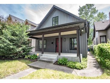 Charming home featuring a covered porch, gray siding, a red door, and lush landscaping at 615 E Morris St, Indianapolis, IN 46203