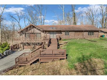 A multi-level brick house showcasing a wooden deck and stairs in a large yard with trees in early spring at 108 Parkridge Dr, Danville, IN 46122