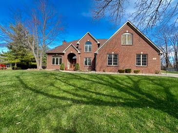 A traditional brick two-story home with a manicured lawn and mature trees under a blue sky at 3610 Eagle Emblem Ct, Greenwood, IN 46143
