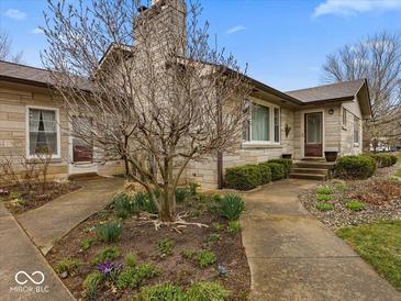 Charming stone home featuring a well-maintained lawn and inviting front entrance with budding spring flowers at 1418 E Maple Dr, Shelbyville, IN 46176