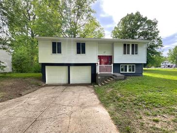 Split-level home featuring a red door and attached two-car garage with a concrete driveway at 2928 Sheffield Dr, Indianapolis, IN 46229