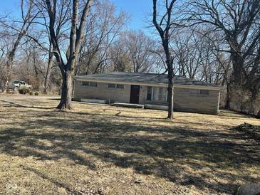 A single story home with a stone facade sits behind trees on a large front lawn at 3817 N Sheridan Ave, Indianapolis, IN 46226