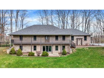 Two-story brick home featuring an upper level deck, lower level patio, and green lawn surrounded by trees at 7023 Mustang Ct, Martinsville, IN 46151