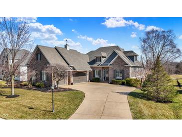 Beautiful stone home with a curved driveway and manicured lawn, accented with lovely trees under a bright blue sky at 16129 Brookhollow Dr, Westfield, IN 46062